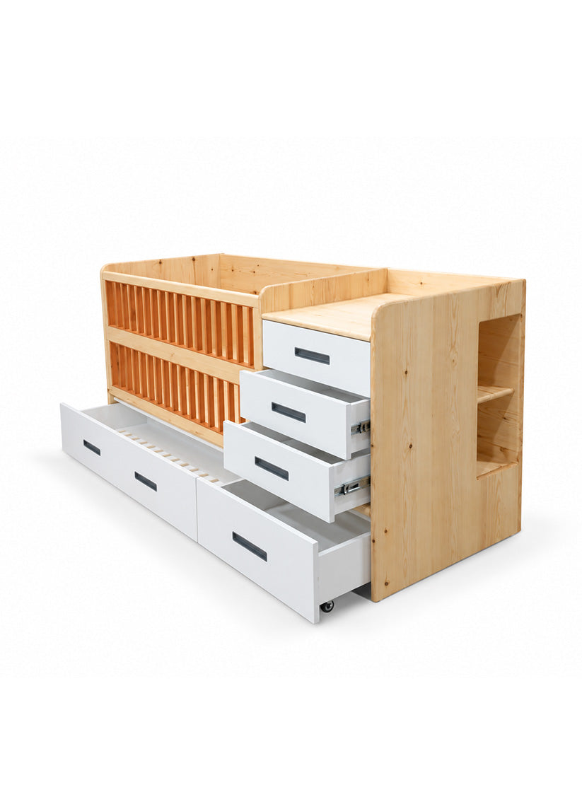 A modern wooden baby bed with a light natural wood frame, a slatted back panel, a built-in shelf, and three white drawers that are partially pulled out, shown on a white background.