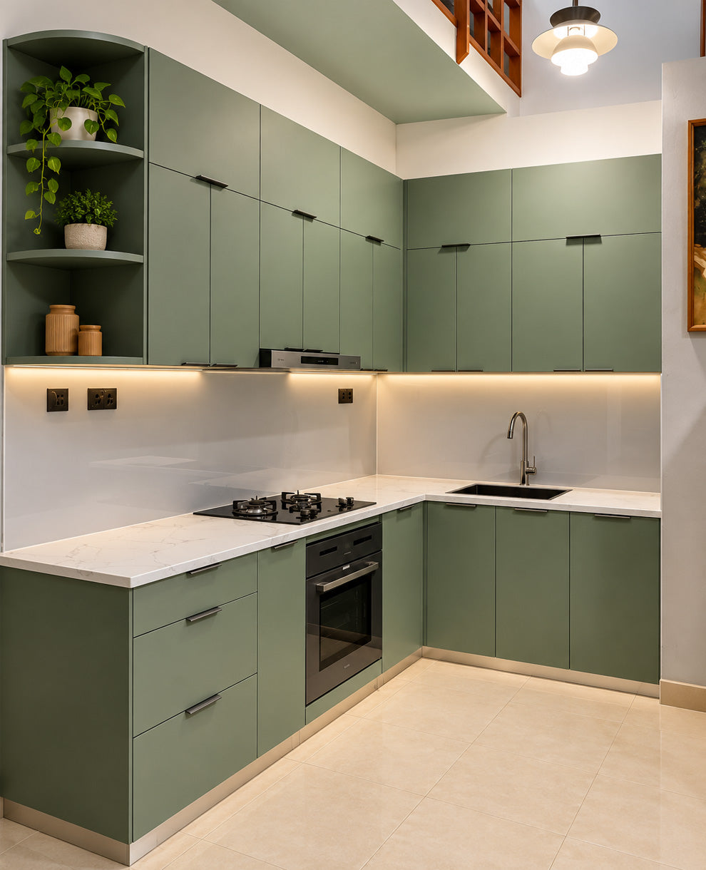 A modern L-shaped kitchen featuring sage green cabinets, white marble countertops, a white backsplash, built-in black appliances, and warm under-cabinet lighting.