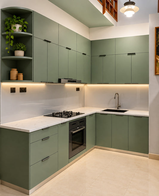 A modern L-shaped kitchen featuring sage green cabinets, white marble countertops, a white backsplash, built-in black appliances, and warm under-cabinet lighting.
