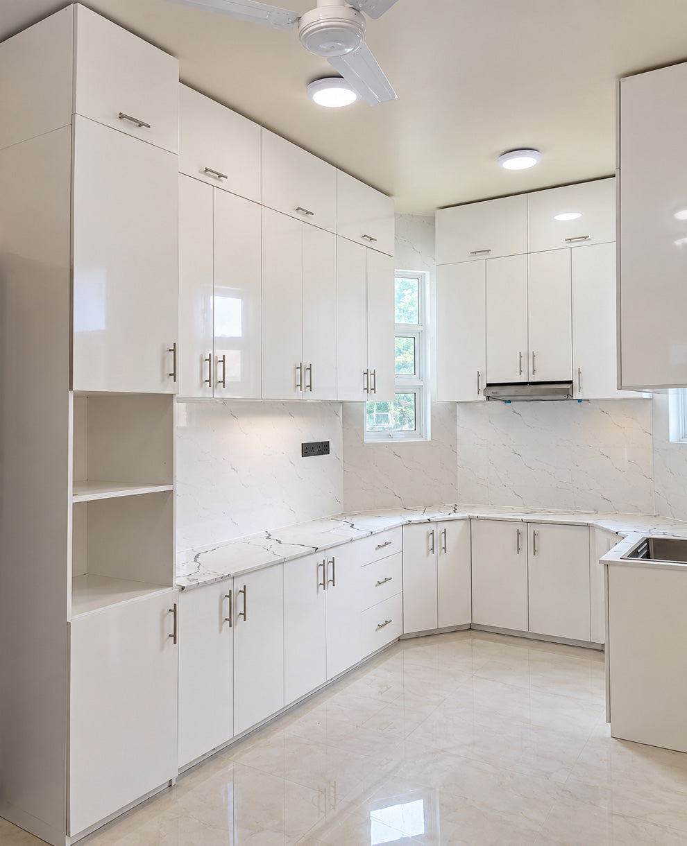 A modern kitchen interior with glossy white cabinetry, marble-look countertops and backsplash, light beige flooring, and recessed ceiling lights.