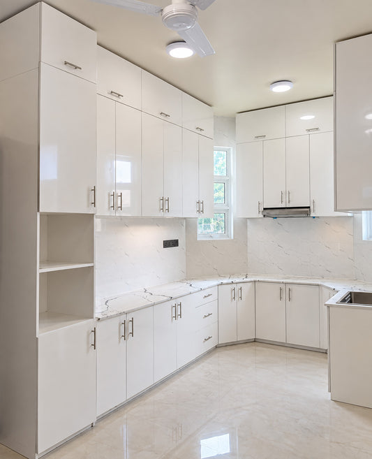 A modern kitchen interior with glossy white cabinetry, marble-look countertops and backsplash, light beige flooring, and recessed ceiling lights.